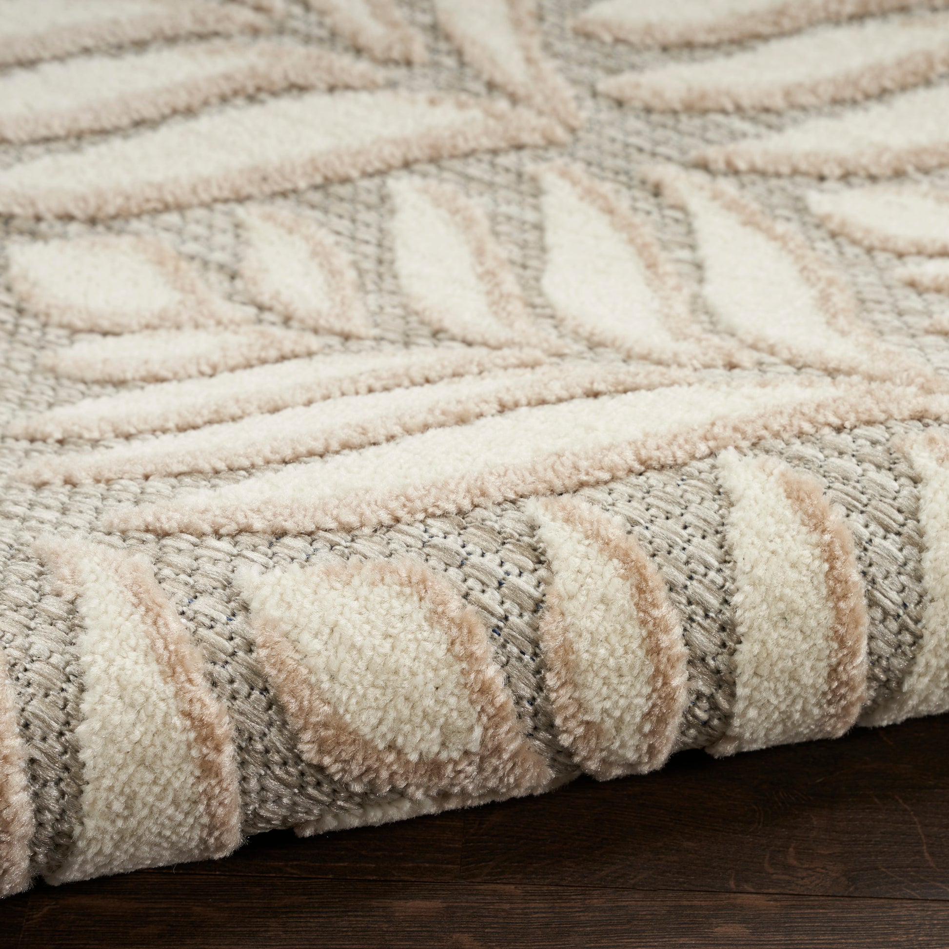 Beige and gray tufted area rug with a raised leaf pattern, soft pile and rolled edge on dark wood floor.