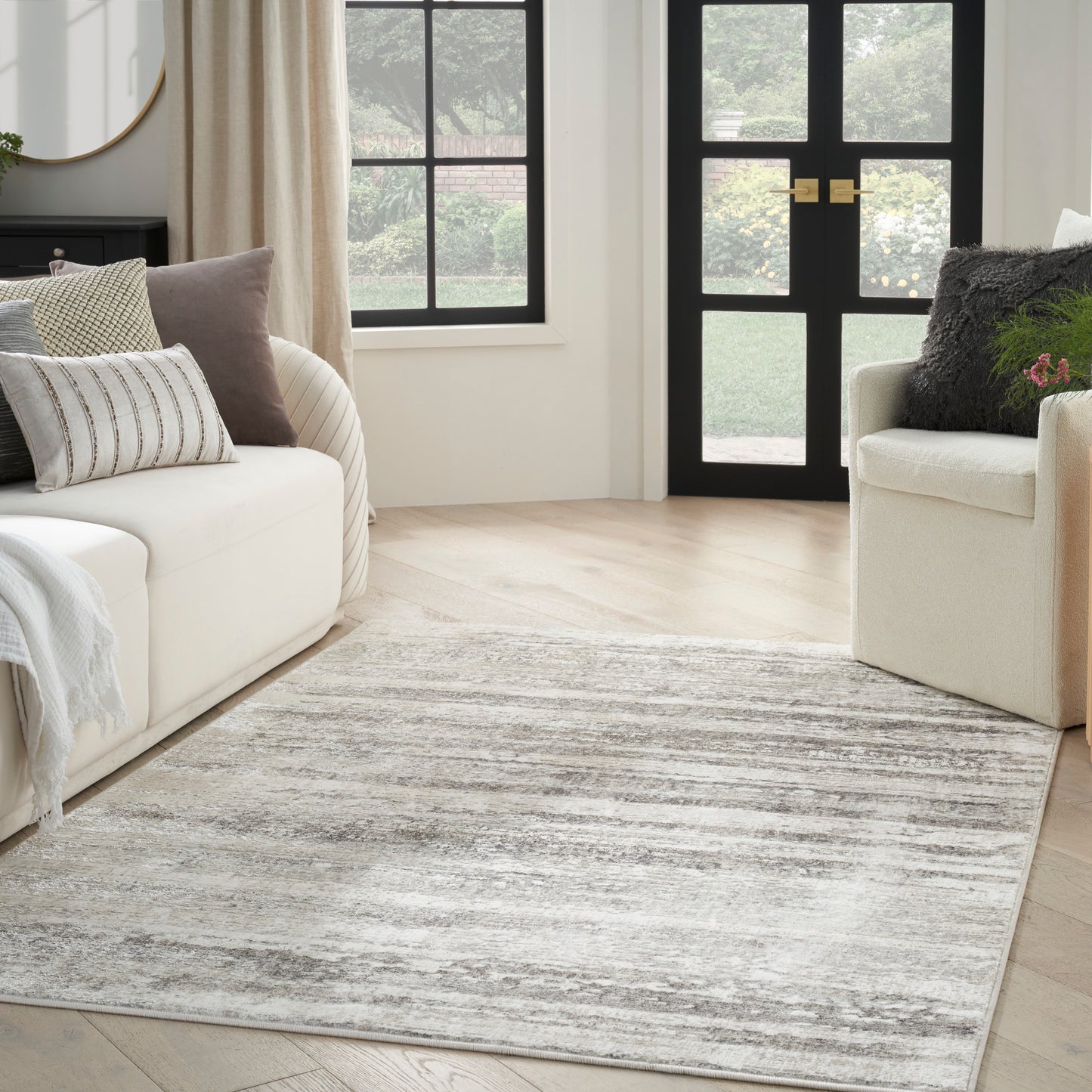 Neutral living room with cream sofa, armchair, light gray striped rug, beige cushions, and black-framed windows and door.