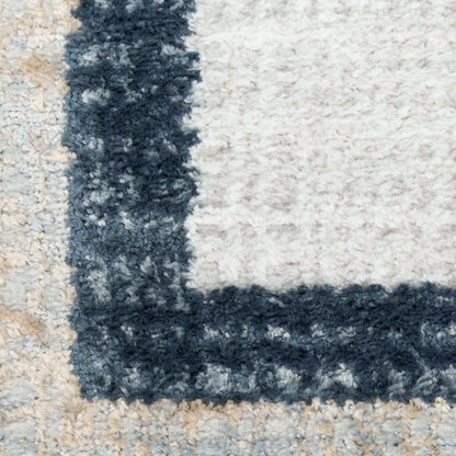 Close-up of a plush rug with navy border against beige and light gray blocks, thick pile texture.