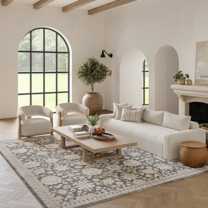 Bright living room with cream sofa, two ivory armchairs, light wood coffee table on a patterned rug; arched window.