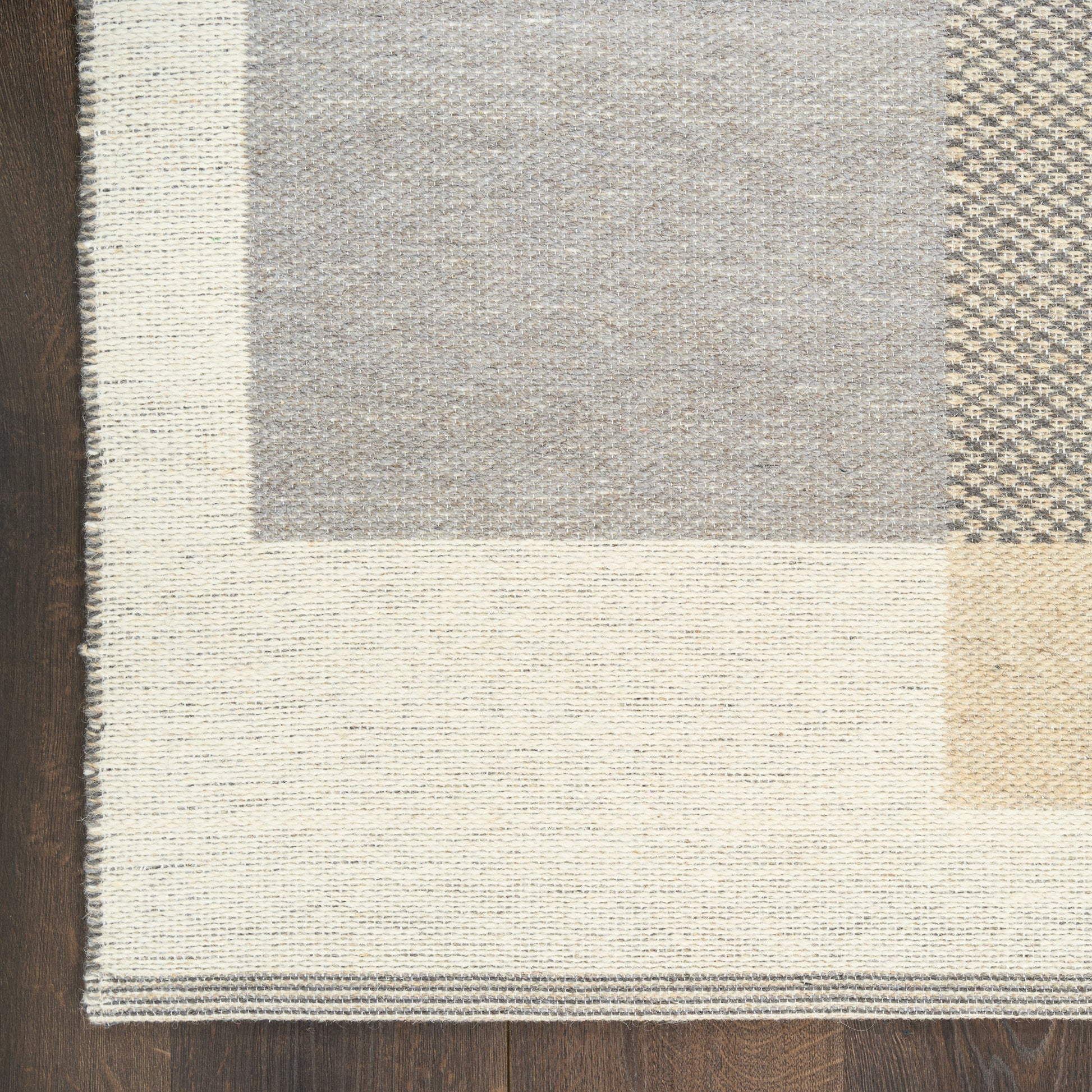 Neutral Mid-Century Modern patchwork rug with cream, taupe and gray woven panels and layered border on wood floor.