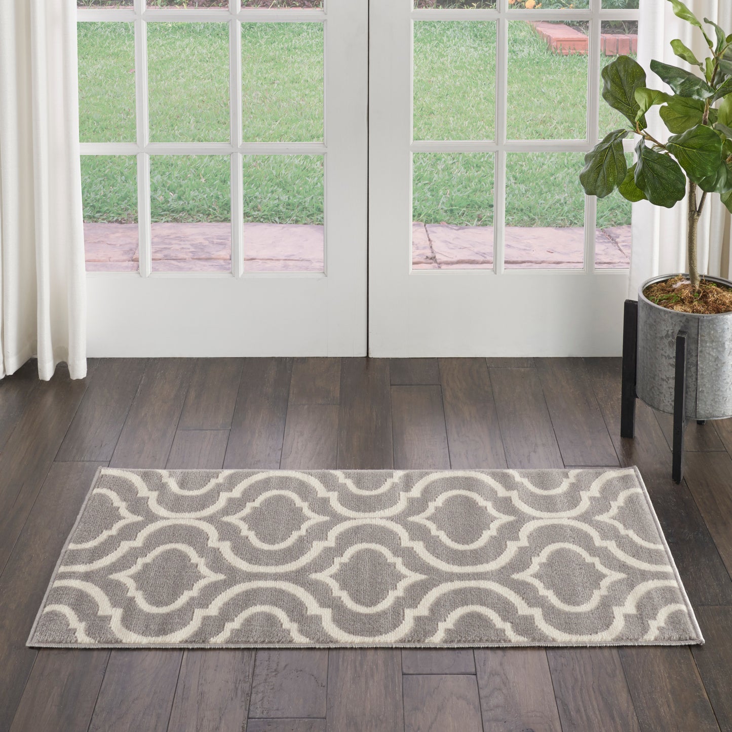 Rectangular gray and white geometric rug with interlocking trellis pattern on dark wood floor by French doors.