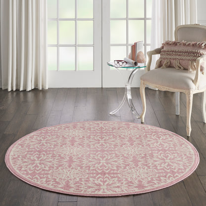 Round pink rug with white floral motif on dark wood floor beside glass side table and cream upholstered armchair.