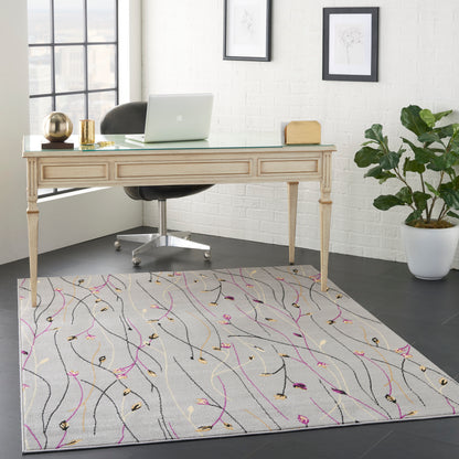 Light carved wood desk with glass top, black chair, gray abstract rug with pink and gold lines, laptop, and plant.