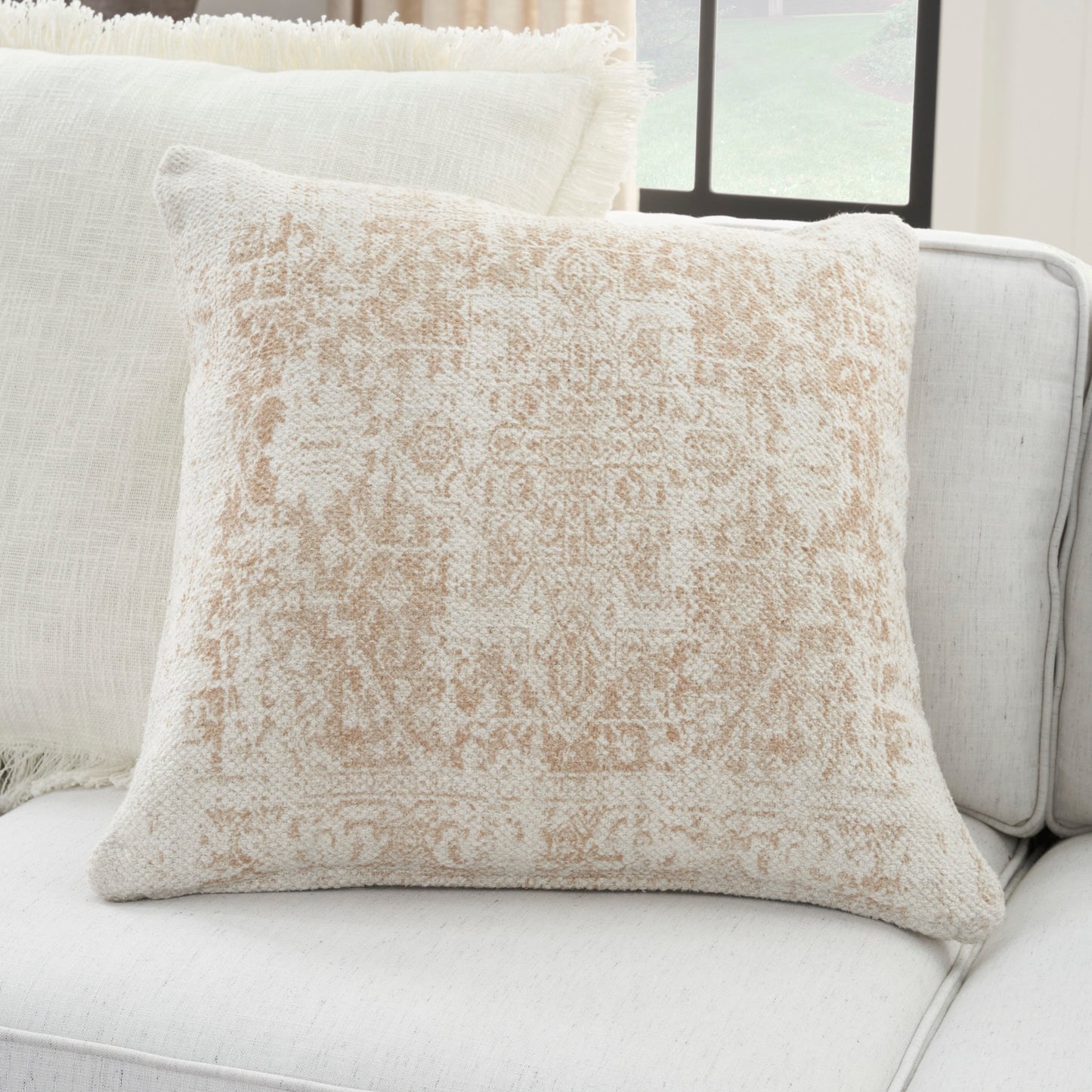 Soft woven beige throw pillow with a faded damask pattern on a light cream sofa.