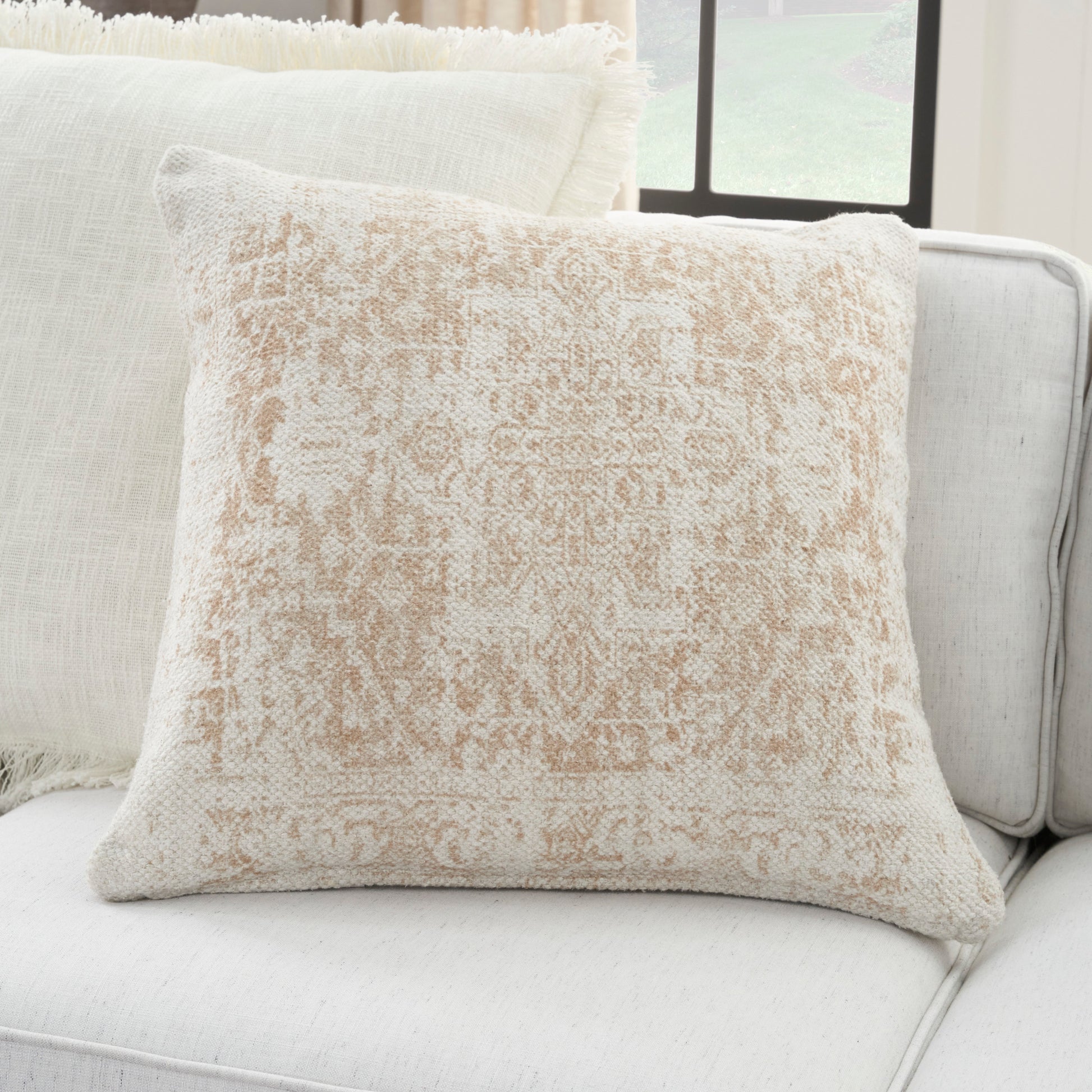 Soft woven beige throw pillow with a faded damask pattern on a light cream sofa.