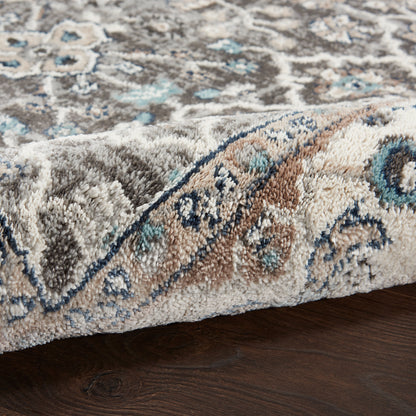 Close-up of an oriental rug with blue, ivory & taupe floral medallion pattern, plush pile, folded edge on dark wood floor.