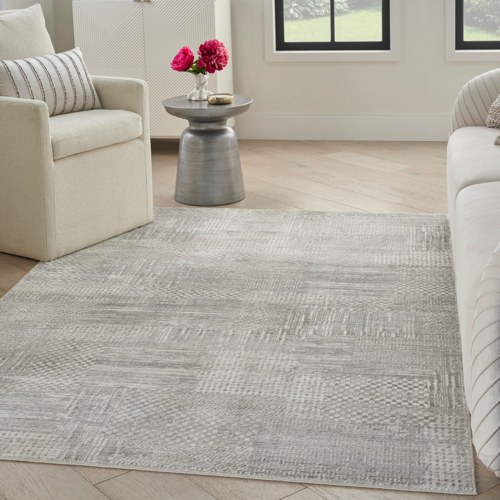 Soft gray textured area rug on wood floor between cream sofas, with a metal side table and pink flowers.