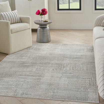 Soft gray textured area rug on wood floor between cream sofas, with a metal side table and pink flowers.