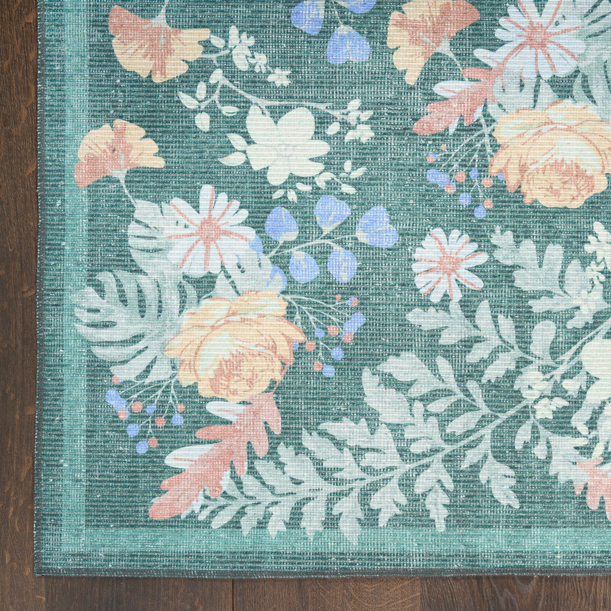 Teal floral area rug with peach and white flowers, lavender accents, woven texture and teal border on wood floor.