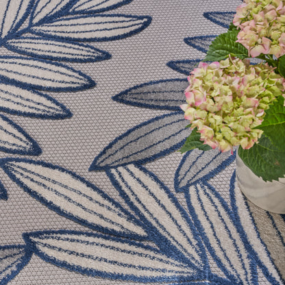 Beige woven rug with bold blue leaf pattern, beside a pink hydrangea bouquet in a white vase.