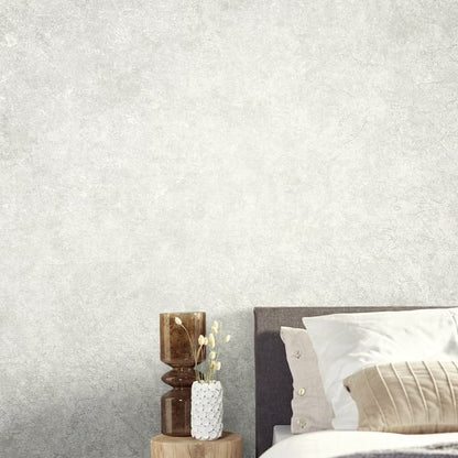 Gray textured wallcovering on the wall in a bedroom scene; round wooden nightstand with brown glass candle holder & white textured vase.