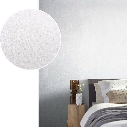 Bedroom scene with silver-grey wallpaper on the wall behind a gray upholstered headboard, beige cushions, and a wooden stump nightstand with a white textured vase.
