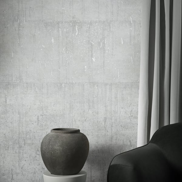 Wallcovering with an aged concrete texture in dark gray; a dark matte ceramic vase sits on a white pedestal beside a black sofa.