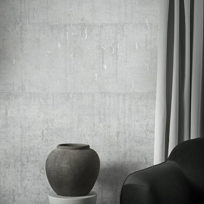 Wallcovering with an aged concrete texture in dark gray; a dark matte ceramic vase sits on a white pedestal beside a black sofa.
