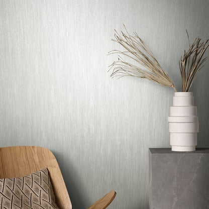 Neutral interior corner with white wallpaper on the walls; wooden chair with a patterned cushion and a stacked white vase with dried pampas grass on a concrete pedestal.