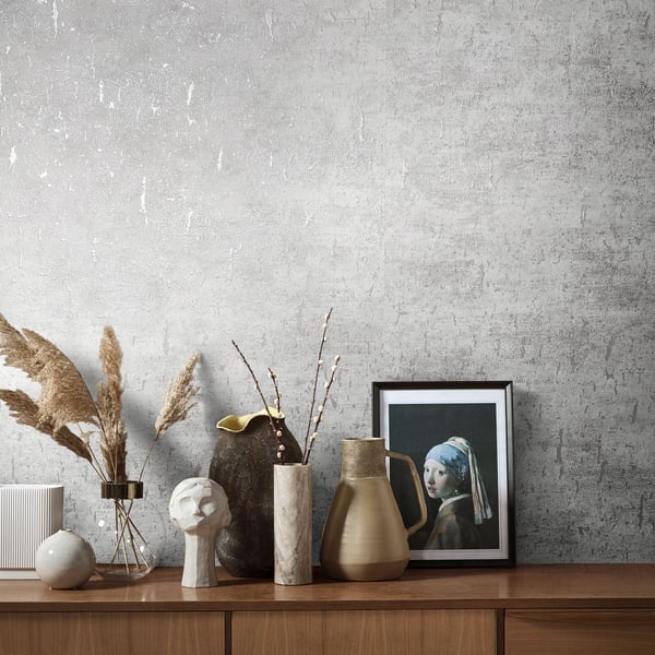 Wallpaper backdrop with a textured gray surface behind a wood mantel displaying ceramic vases, a plaster bust, pampas grass, a ceramic jug, and framed art.