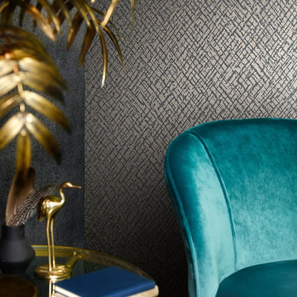 Gold crosshatch wallpaper backdrop with a teal velvet curved chair and a gold side table set with a blue book, a golden flamingo statue, and tropical leaves.