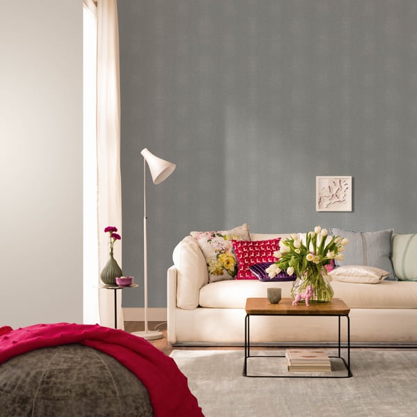 Cozy living room with blue-gray wallpaper on the wall, white sofa, wooden coffee table, vase of tulips, white floor lamp, and pink throw.