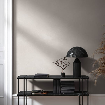 Black metal two-shelf console against beige wall with veined black glass dome lamp, black tree sculpture, and dark books.