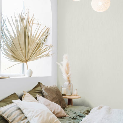 White textured wallpaper on the wall of a boho bedroom; visible decor includes a dried palm by the window, beige-green pillows, woven textiles, and a wooden side table.