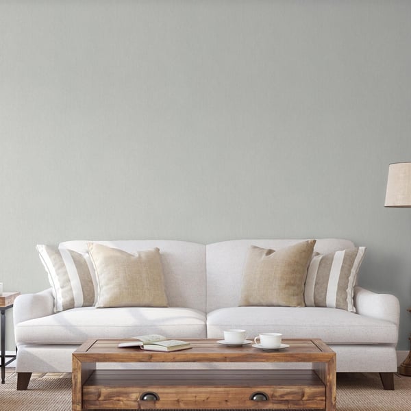 Neutral living room with light grey wallpaper featuring a subtle silver-grey stripe; beige and striped pillows on a light grey fabric sofa; wooden coffee table with cups and a book on a rug.