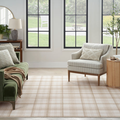 Sunlit living room with green velvet sofa, light gray striped chair, beige plaid rug, wooden side table & potted plants.