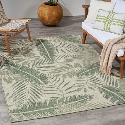 Flat-weave area rug with green palm leaf pattern on beige in a modern living room with wooden chair, sofa, and a terracotta planter.