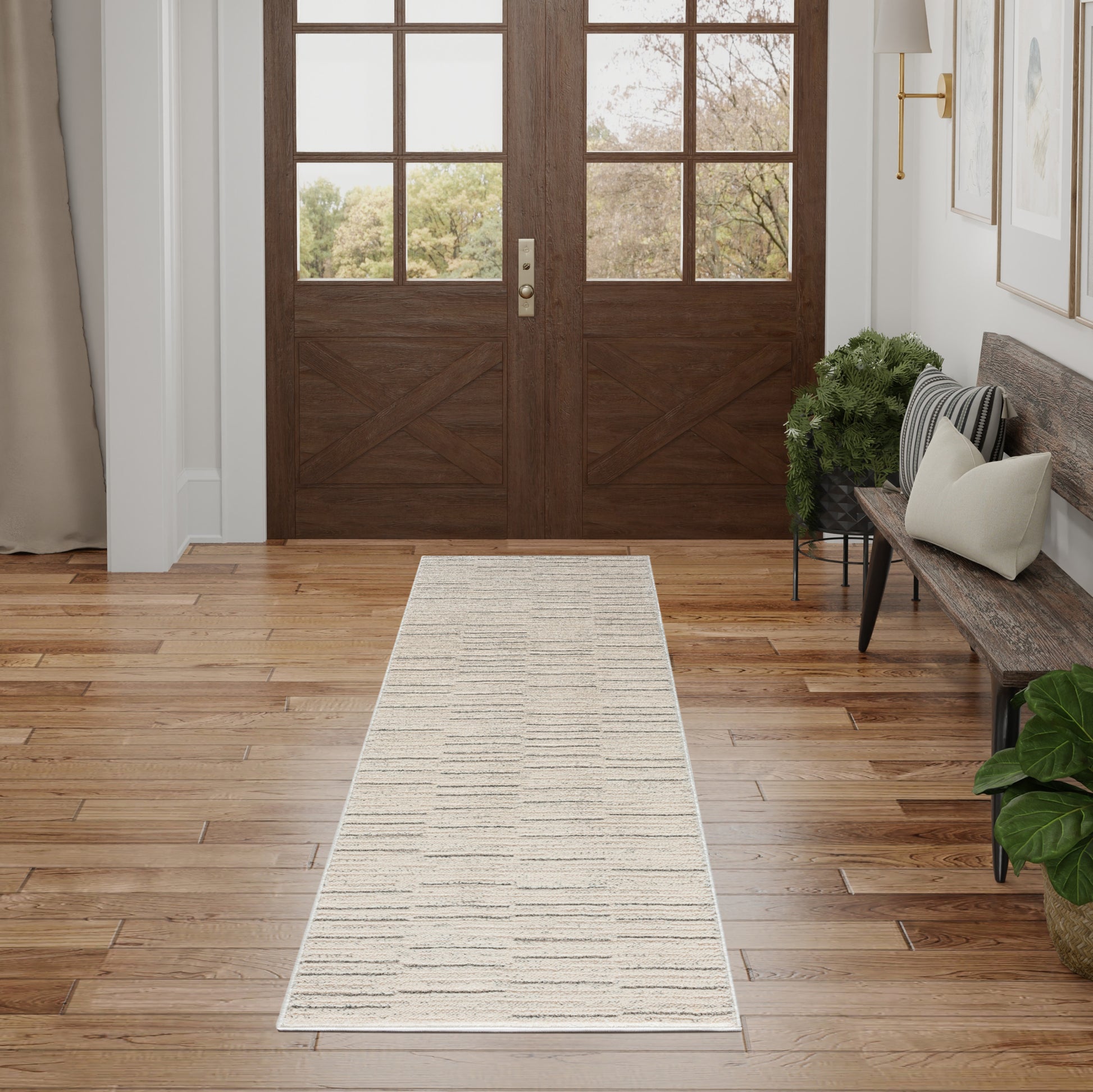 Long beige striped runner rug in a warm hardwood entryway with dark wood double doors, a bench with cushions and a potted plant.