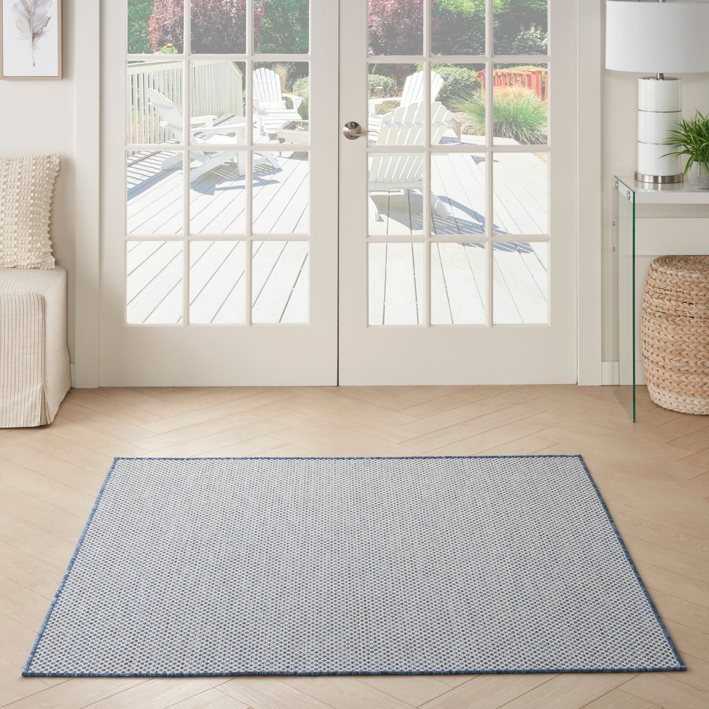 Rectangular light blue patterned area rug with a thin blue border on a light wood floor in front of glass French doors.