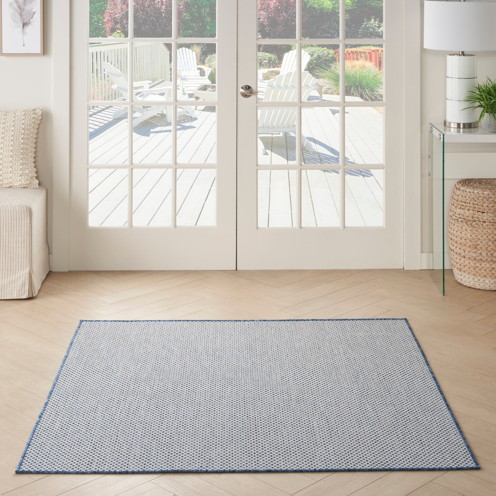 Rectangular light blue patterned area rug with a thin blue border on a light wood floor in front of glass French doors.