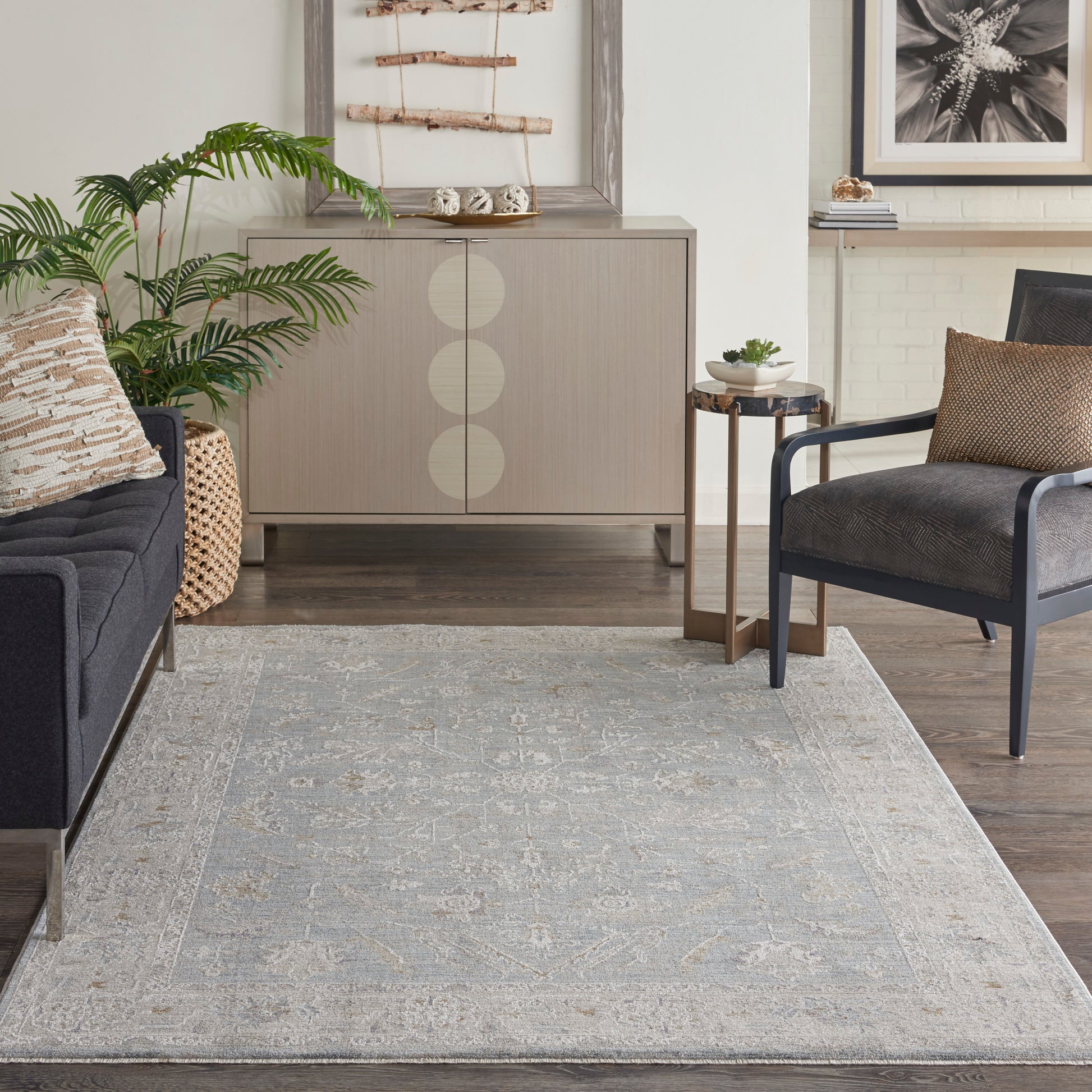 Contemporary living room with a taupe cabinet featuring circular doors, gray-blue traditional rug, navy chair, and dark gray sofa.