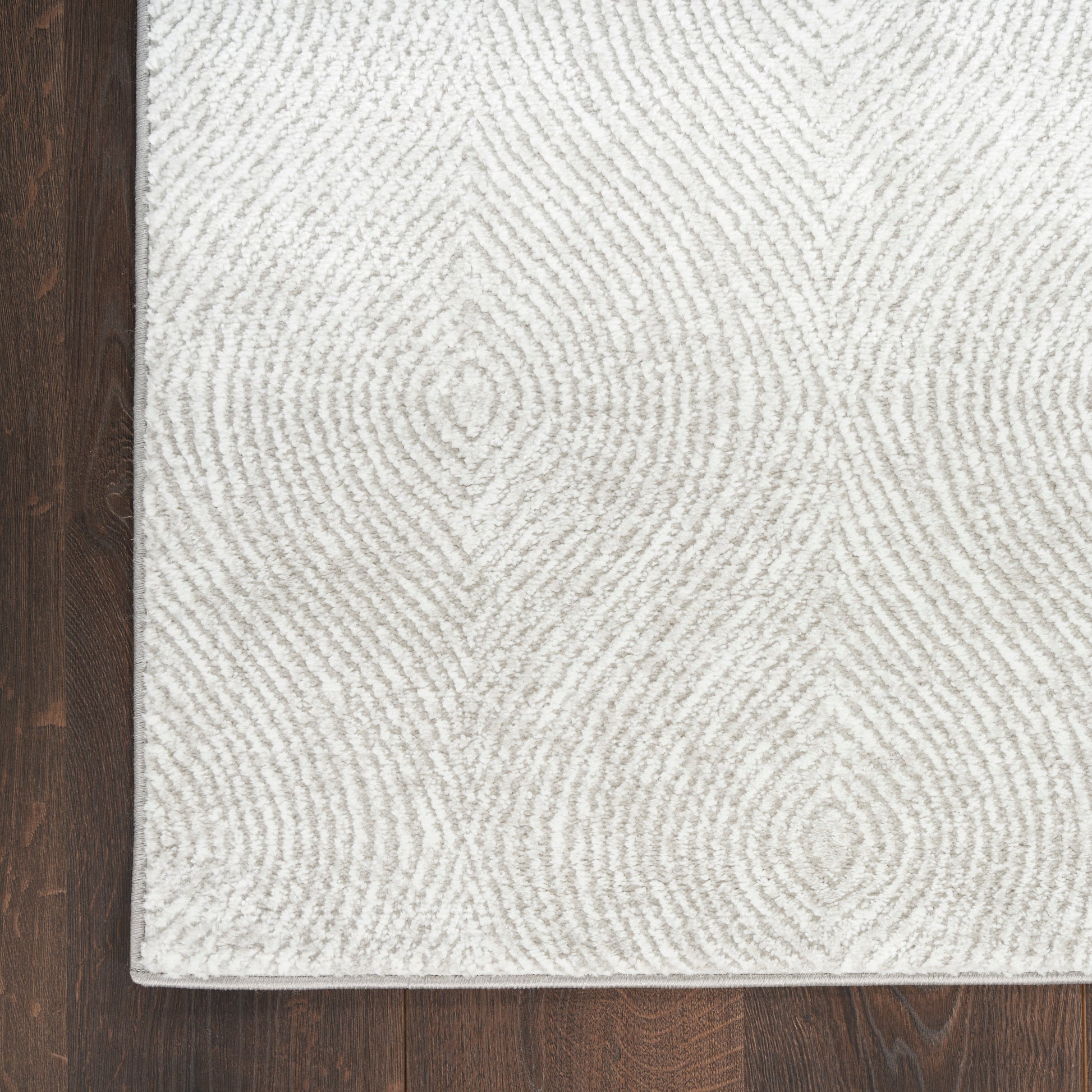 Cream textured area rug with soft gray fingerprint-like concentric rings, set on dark wood flooring.