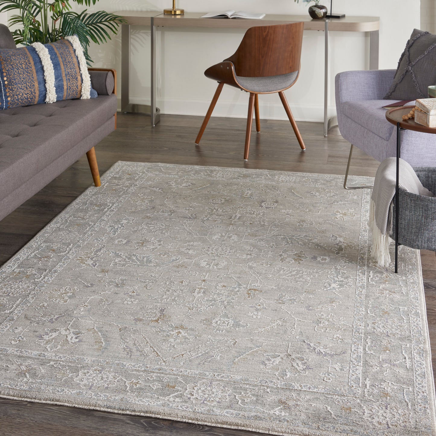 Light gray patterned area rug in a contemporary living room with a gray sofa, blue pillows, and a mid-century wooden chair.