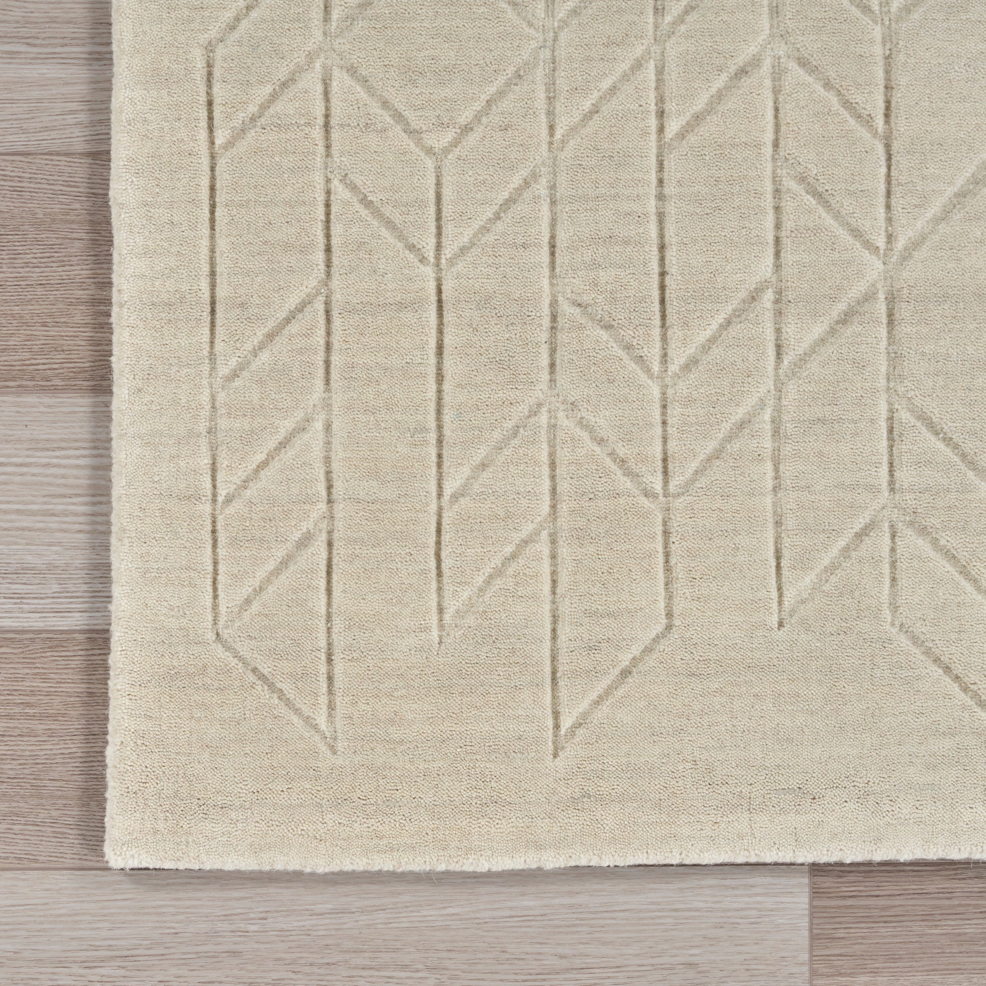 Beige textured rug with raised geometric chevron and diamond pattern on light wood floor.