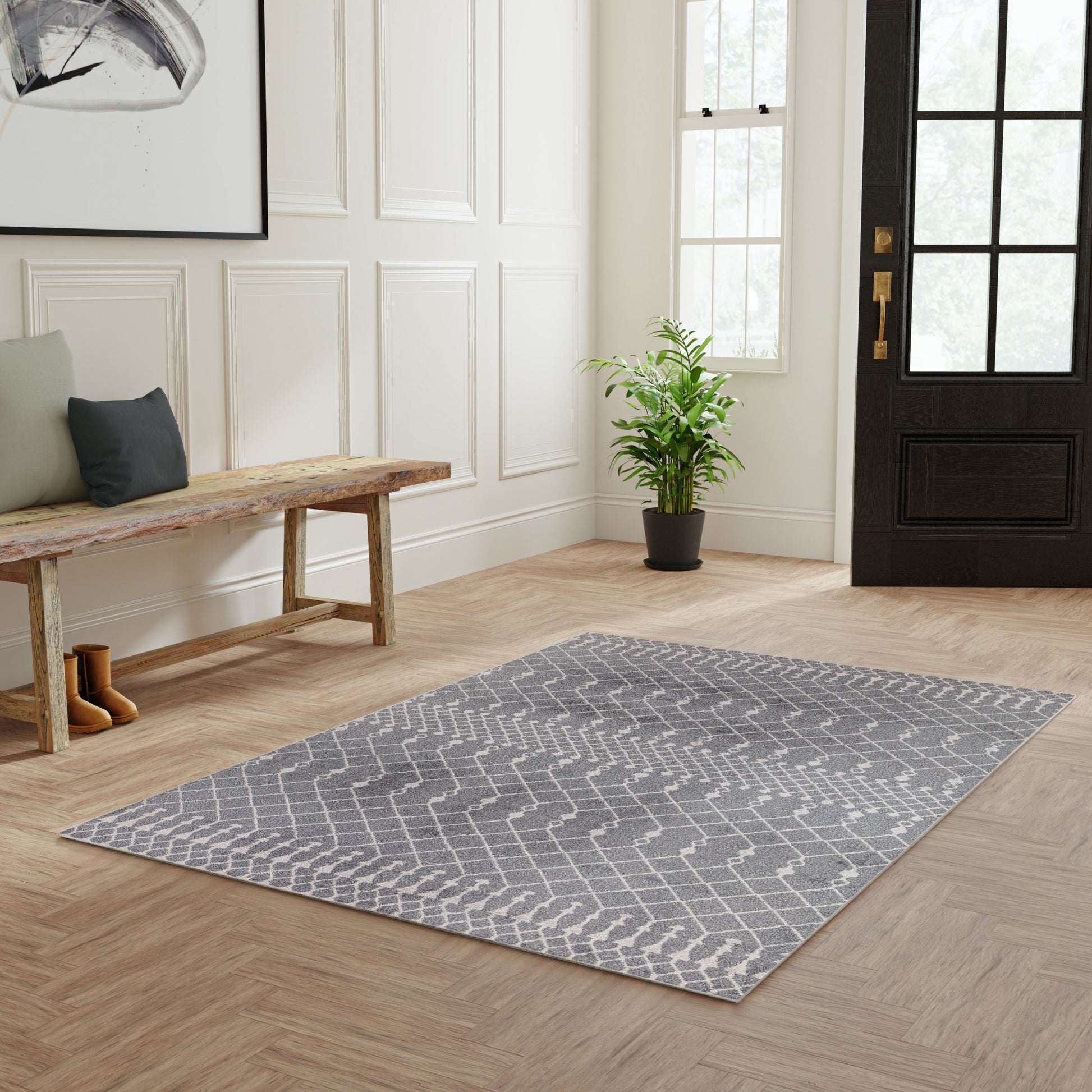 Entryway with white paneled walls, gray chevron rug, wooden bench, plant, and dark front door with glass panes.