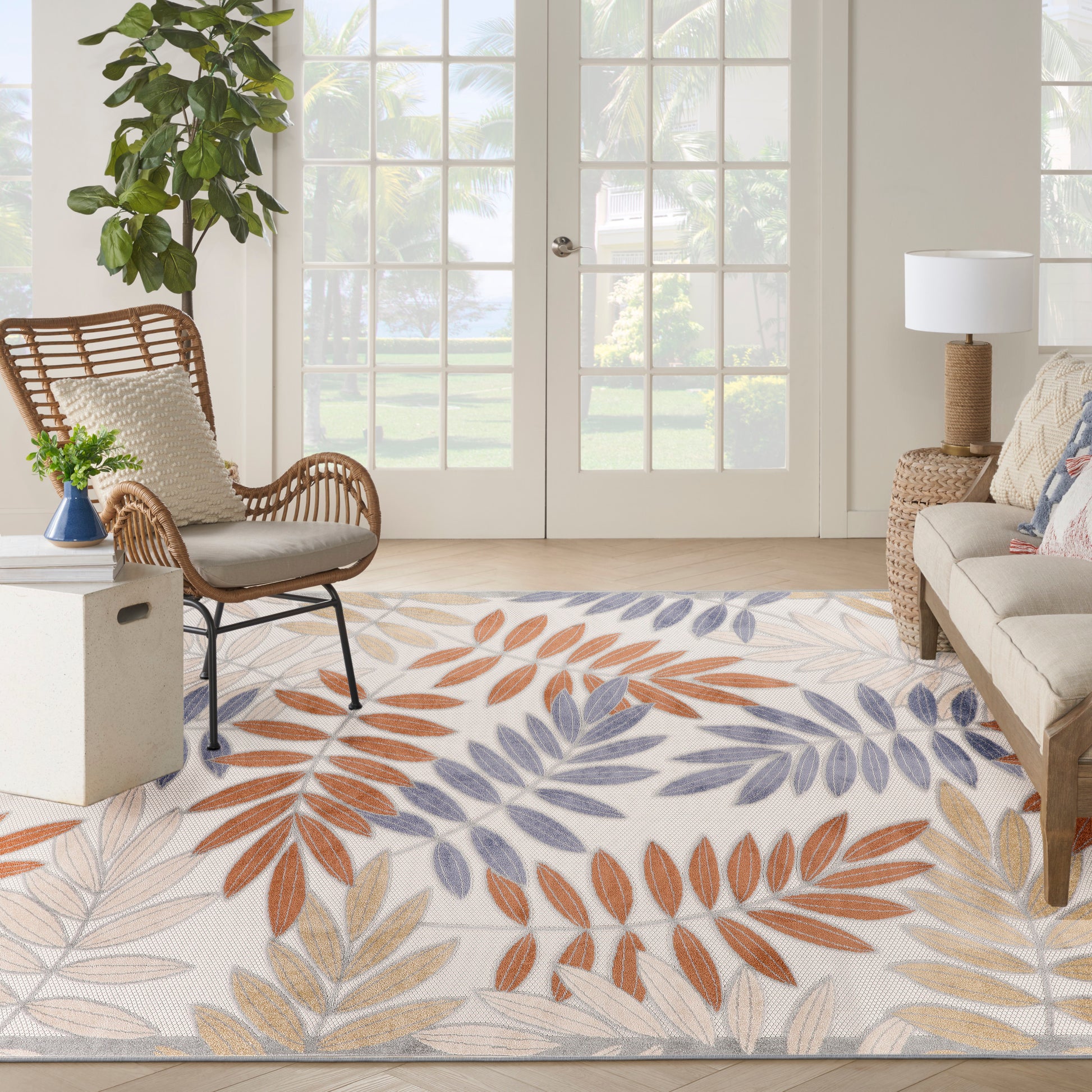 Bright outdoor space with a leaf-pattern rug in orange, blue, and beige, a rattan chair, plants, and glass patio doors.