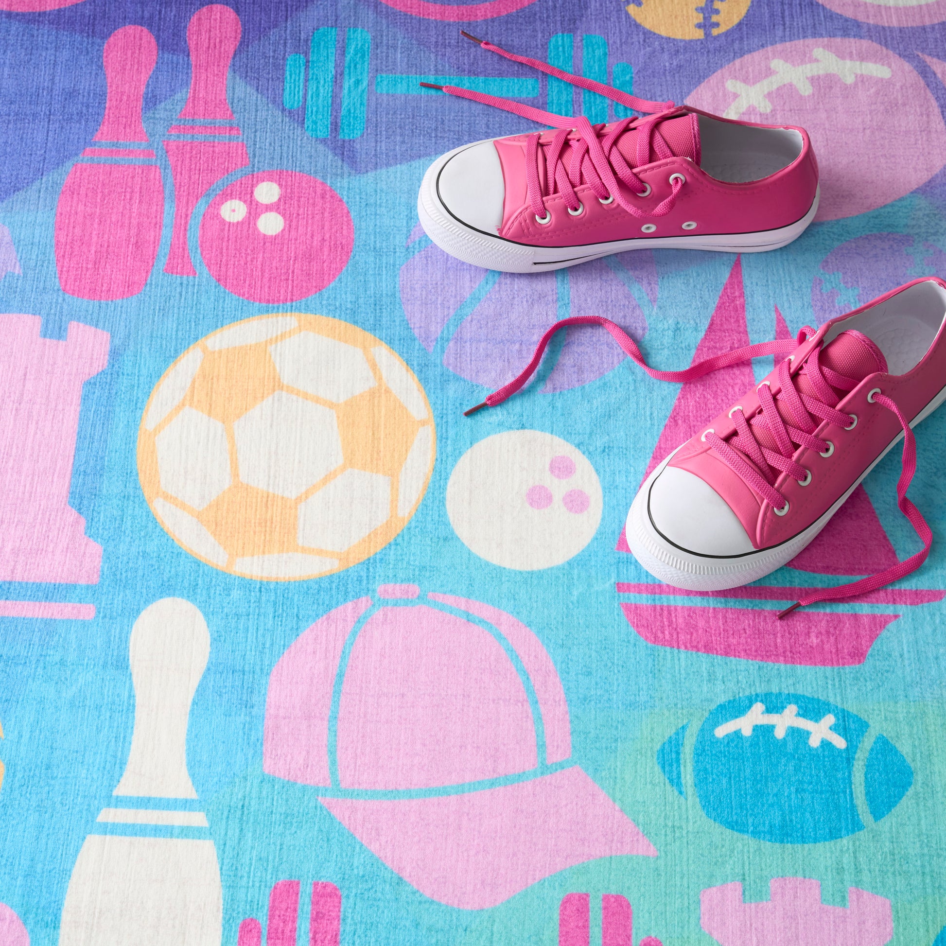 Pink canvas low-top sneakers with white rubber toe caps and laces on a colorful sports-themed mat.