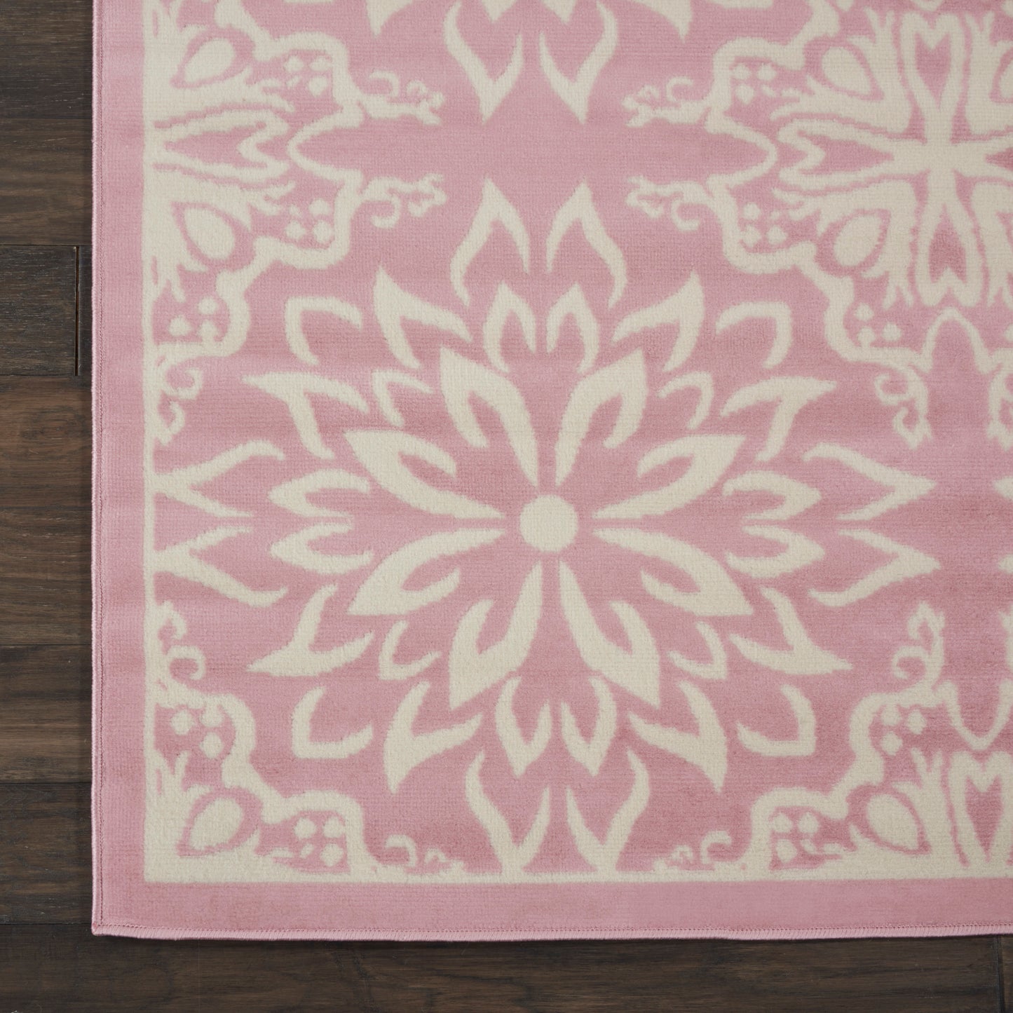 Pink area rug featuring a white mandala floral pattern and border on dark wood floor.