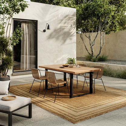 Modern outdoor dining set: natural wood table with black metal legs, tan woven wicker chairs, on a beige rug in a sunny courtyard.