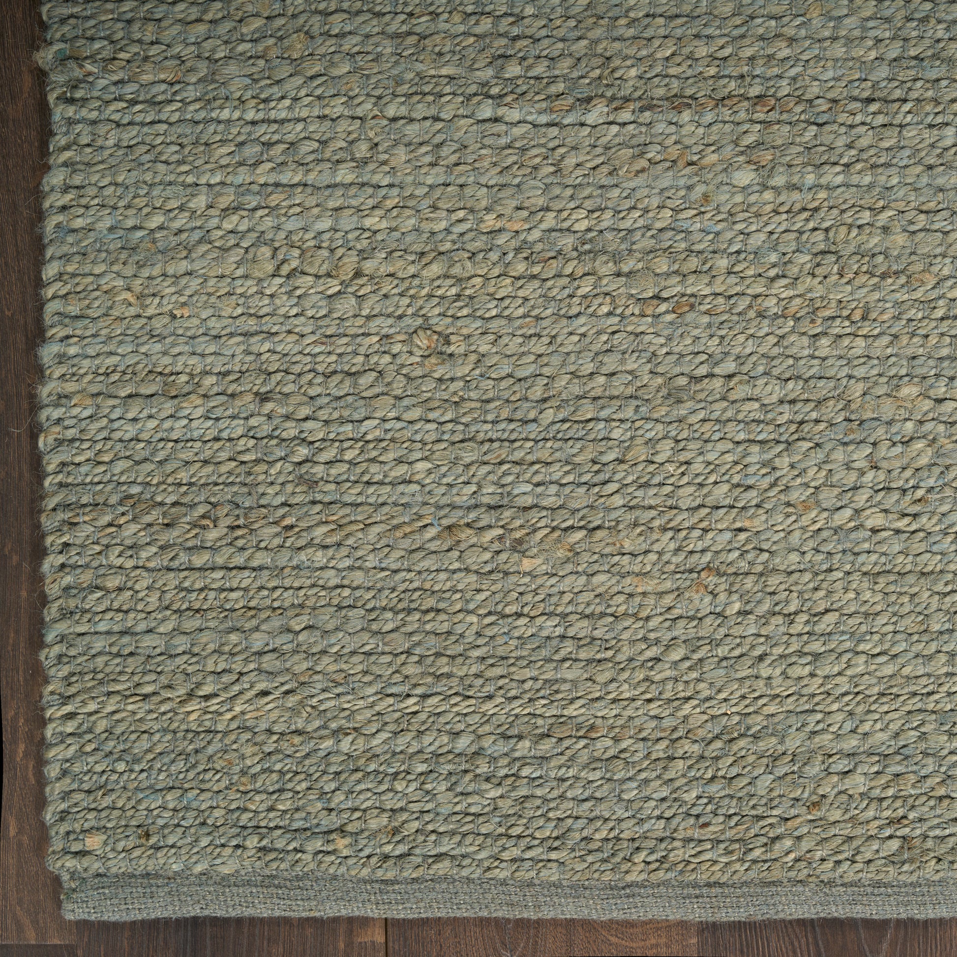Close-up of a greenish-blue loop-pile rug on wooden floor with a dark border edge.