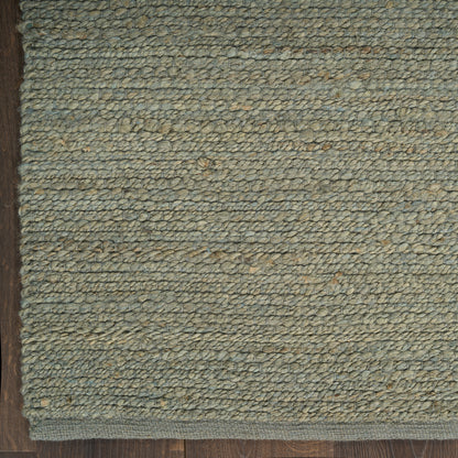 Close-up of a greenish-blue loop-pile rug on wooden floor with a dark border edge.