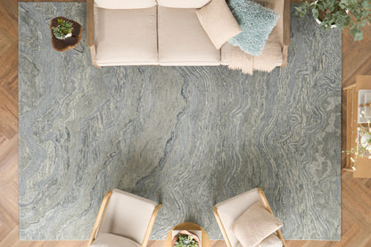 Top-down view of a living room: gray-blue marbled rug, beige sofa, two light-wood chairs, and potted plants.