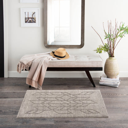 Beige tufted bench with dark wood legs, draped throw, straw hat, rounded mirror, vase & branches, gray geometric rug.