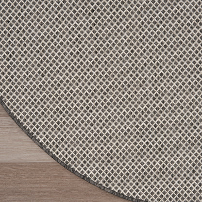 Round, flat-weave rug with beige and charcoal diamond lattice pattern and dark edge, laid on wood floor.