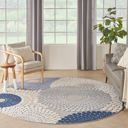 Round blue and white rug with concentric dot pattern in a bright living room with sofa, wooden chair, plant and large windows.
