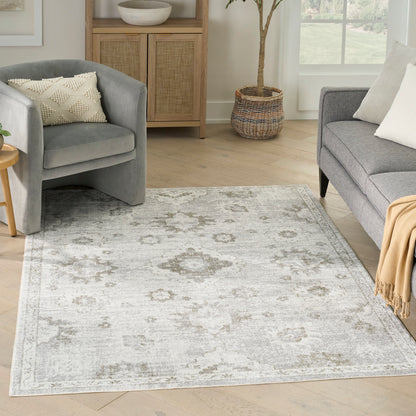 Light gray patterned area rug in a cozy living room with gray upholstered chairs, beige throw, and wooden cabinet.