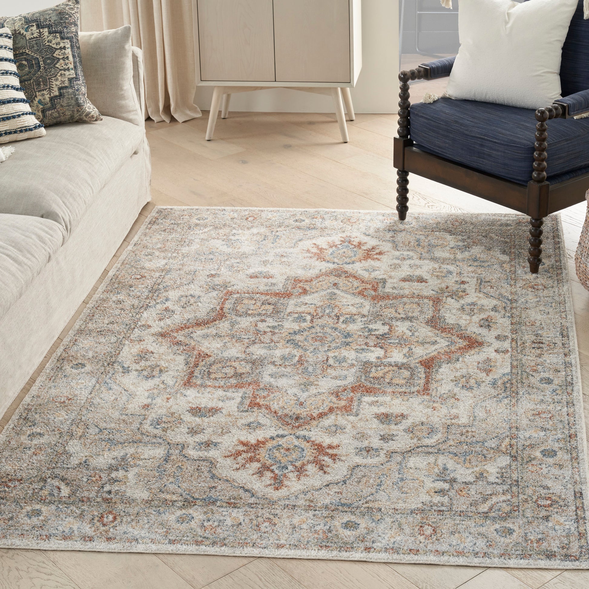 Beige oriental rug with blue and rust geometric motif on light wood floor; beige sofa left and navy chair right.