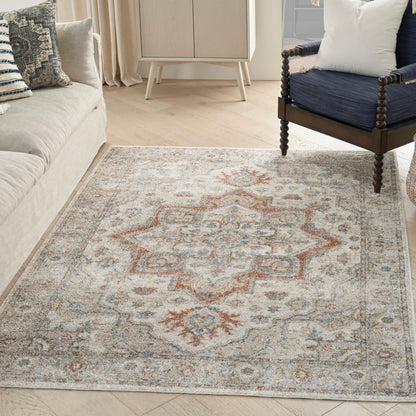 Beige oriental rug with blue and rust geometric motif on light wood floor; beige sofa left and navy chair right.
