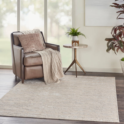 Beige area rug in a living room scene featuring a brown leather armchair, beige knitted throw, pillow, and a round wood side table.